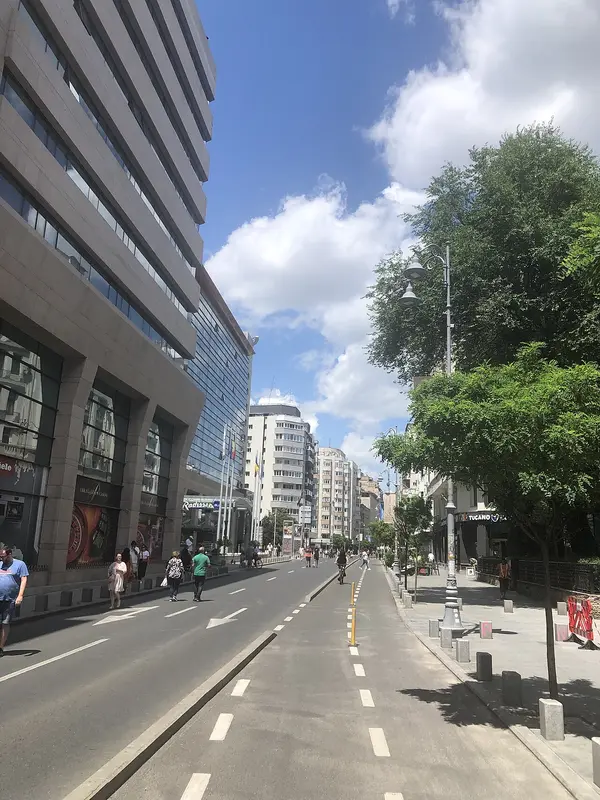 Pedestrians stroll along Calea Victoriei in Bucharest on a sunny day, the broad avenue lined with trees and grand facades